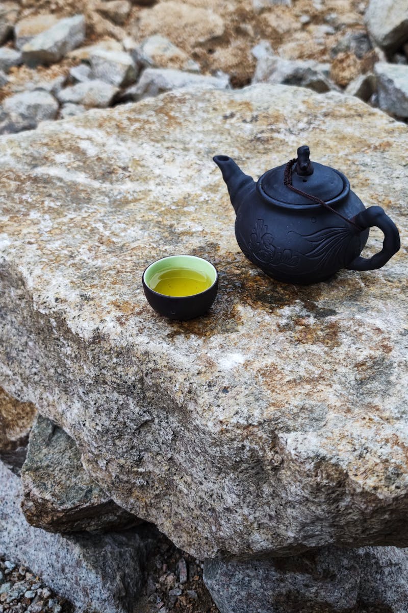 A traditional black teapot and cup with tea placed on a natural stone surface outdoors in Vietnam.